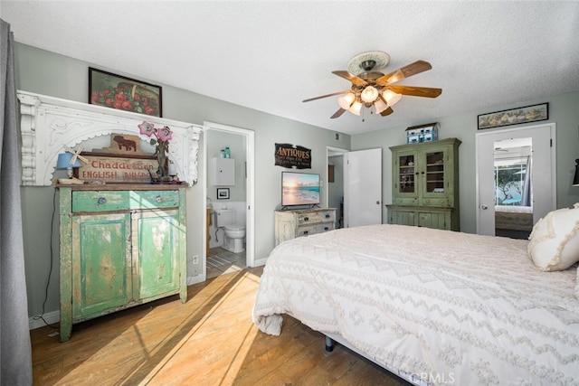 bedroom featuring baseboards, a ceiling fan, ensuite bath, wood finished floors, and a textured ceiling