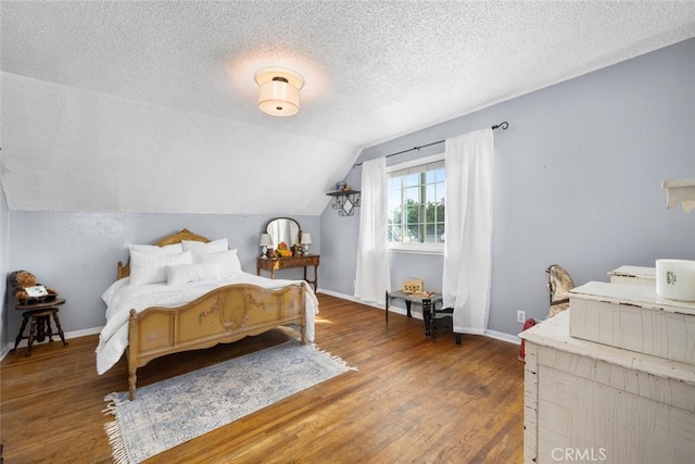 bedroom featuring lofted ceiling, a textured ceiling, baseboards, and wood finished floors