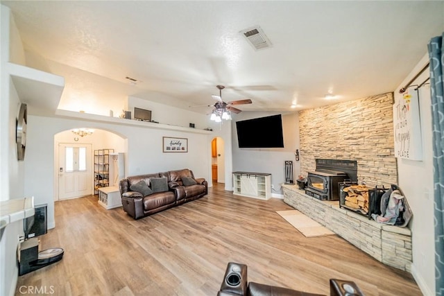 living room featuring a ceiling fan, visible vents, wood finished floors, a wood stove, and arched walkways