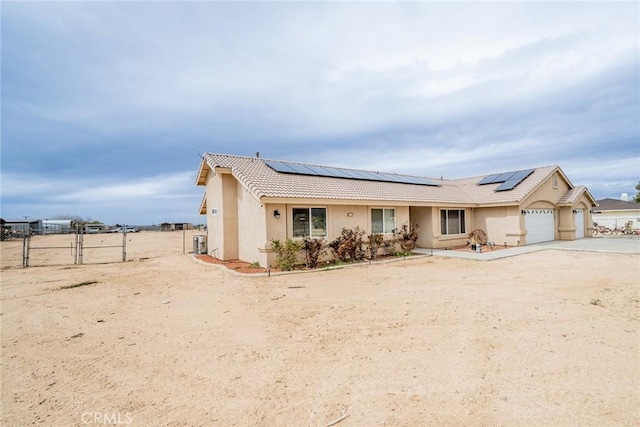 view of front of home with fence, driveway, stucco siding, a garage, and roof mounted solar panels