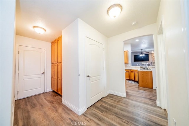 hallway featuring arched walkways, baseboards, and wood finished floors