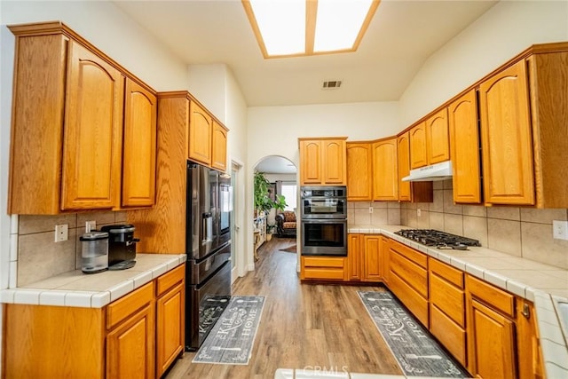 kitchen featuring visible vents, light wood-style flooring, arched walkways, under cabinet range hood, and appliances with stainless steel finishes