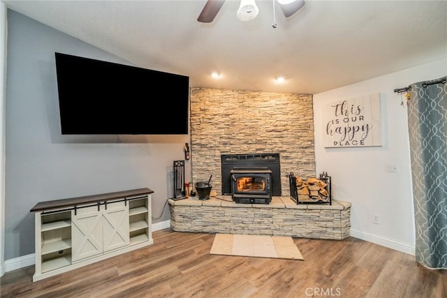 living room featuring wood finished floors, baseboards, ceiling fan, a wood stove, and vaulted ceiling