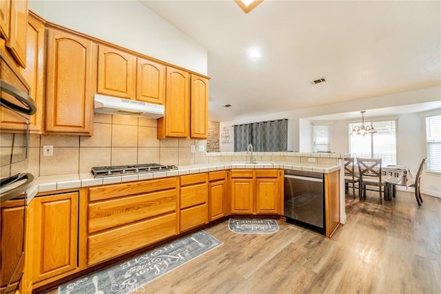 kitchen with visible vents, under cabinet range hood, a sink, appliances with stainless steel finishes, and a peninsula