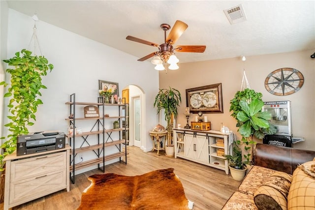 living room with a ceiling fan, baseboards, visible vents, arched walkways, and light wood-type flooring