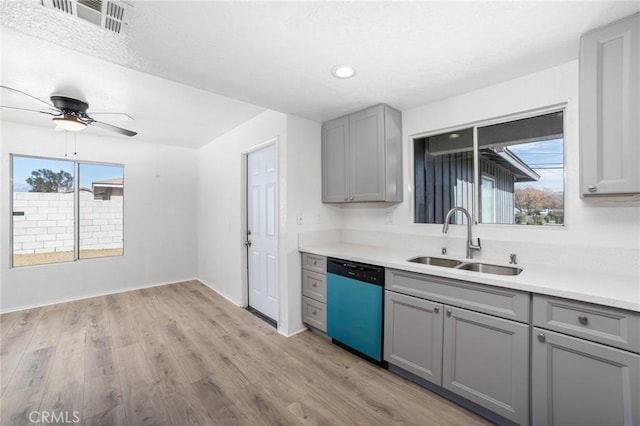 kitchen with a sink, dishwashing machine, gray cabinets, and light wood-style floors