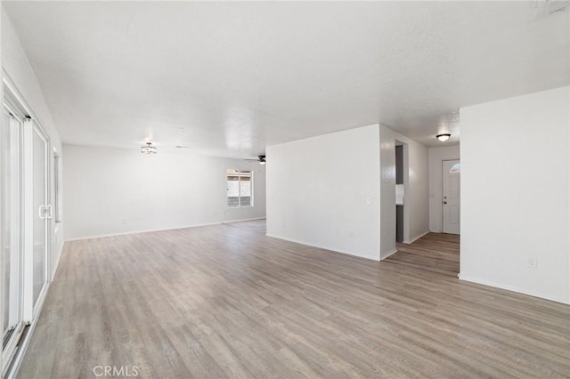 unfurnished living room featuring ceiling fan, baseboards, and light wood-style floors