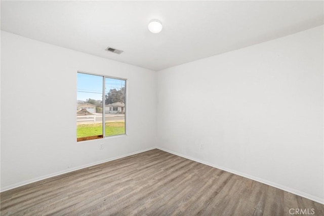 unfurnished room featuring baseboards, visible vents, and wood finished floors