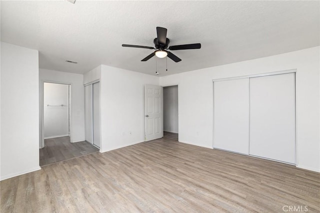 unfurnished bedroom featuring a textured ceiling, ceiling fan, multiple closets, and light wood-style floors