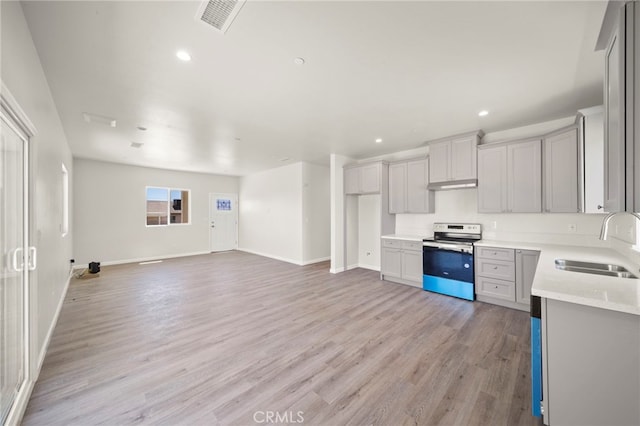 kitchen featuring light countertops, a sink, stainless steel range with electric stovetop, light wood-type flooring, and under cabinet range hood