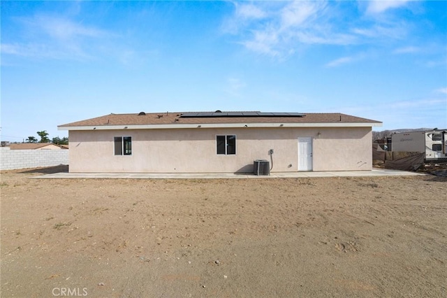 rear view of house with central air condition unit, roof mounted solar panels, fence, and stucco siding