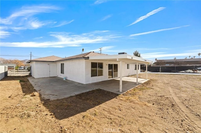 rear view of house featuring a patio area, fence, and stucco siding