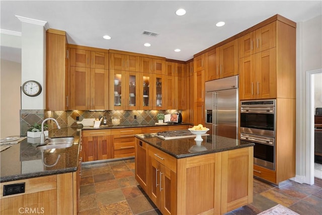 kitchen featuring stone tile floors, stainless steel appliances, backsplash, a sink, and dark stone countertops