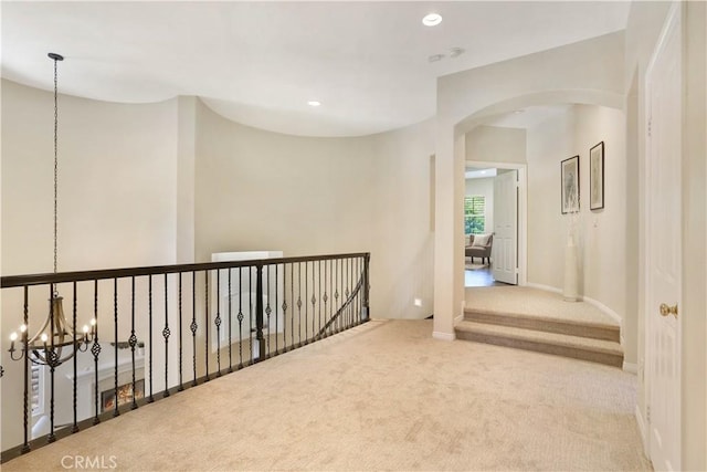 corridor featuring baseboards, arched walkways, carpet floors, a notable chandelier, and recessed lighting