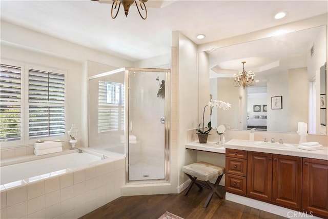 ensuite bathroom featuring a chandelier, a garden tub, wood finished floors, vanity, and a stall shower