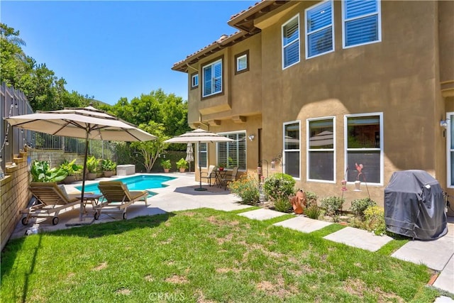 rear view of property featuring a patio, fence, a lawn, a fenced in pool, and stucco siding