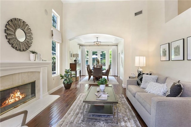 living area with baseboards, visible vents, a tiled fireplace, wood finished floors, and a high ceiling