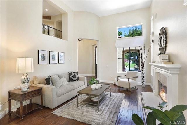 living area with visible vents, a towering ceiling, dark wood-type flooring, a lit fireplace, and baseboards