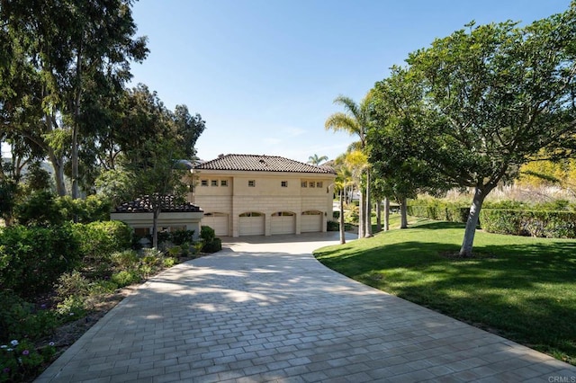view of front of home featuring a tile roof, decorative driveway, a front lawn, and a garage