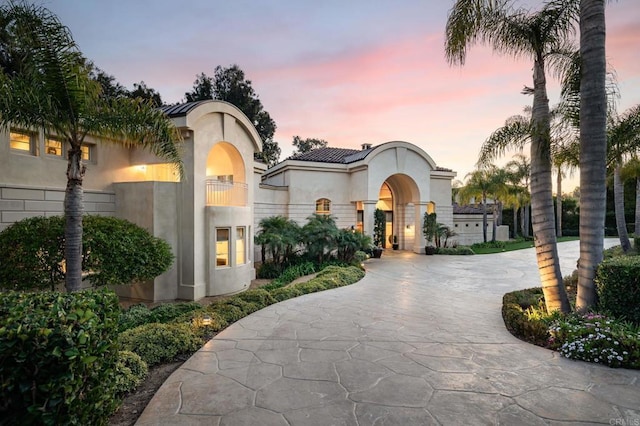 mediterranean / spanish home with stucco siding, a tiled roof, and curved driveway