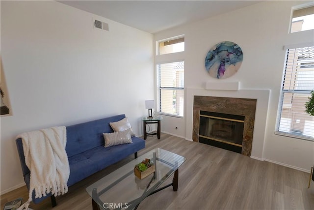 living area with a fireplace, visible vents, a wealth of natural light, and wood finished floors