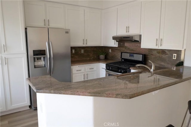 kitchen with under cabinet range hood, stone counters, appliances with stainless steel finishes, and white cabinets