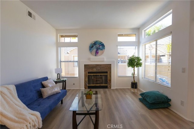 living room with a healthy amount of sunlight, visible vents, wood finished floors, and a high end fireplace