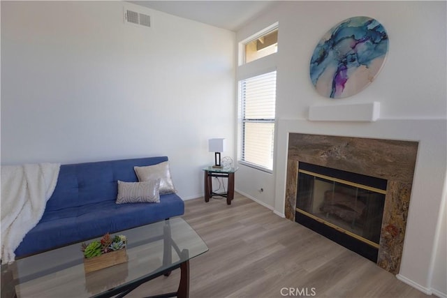 living area with a high end fireplace, visible vents, baseboards, and wood finished floors