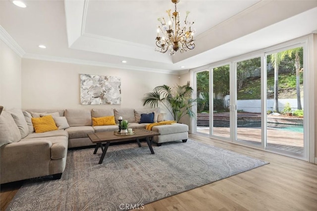 living area featuring a notable chandelier, recessed lighting, wood finished floors, ornamental molding, and a raised ceiling