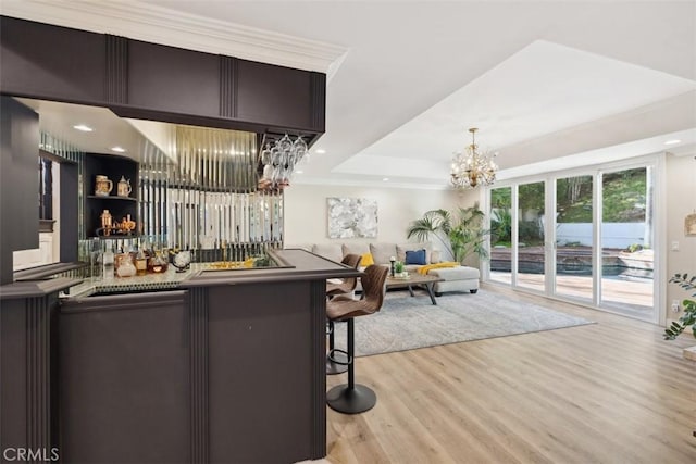 bar featuring a chandelier, recessed lighting, light wood-style floors, wet bar, and a raised ceiling