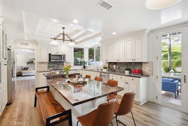 kitchen with visible vents, decorative backsplash, a breakfast bar area, appliances with stainless steel finishes, and a tray ceiling