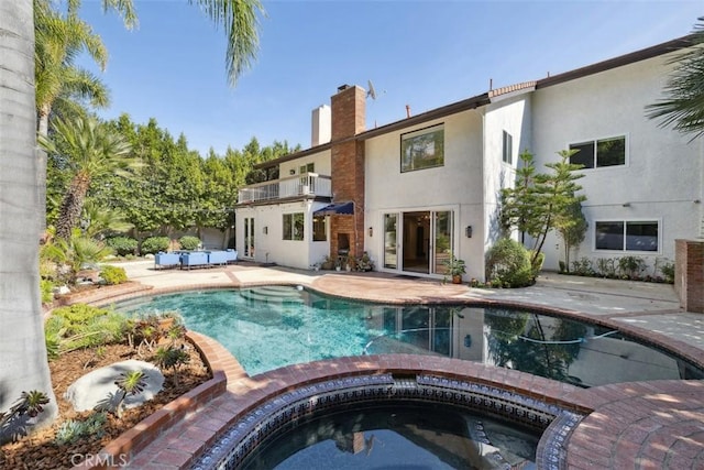 back of house with a patio, stucco siding, a balcony, an in ground hot tub, and an outdoor pool