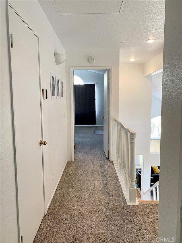 hall with carpet flooring, a textured ceiling, and baseboards