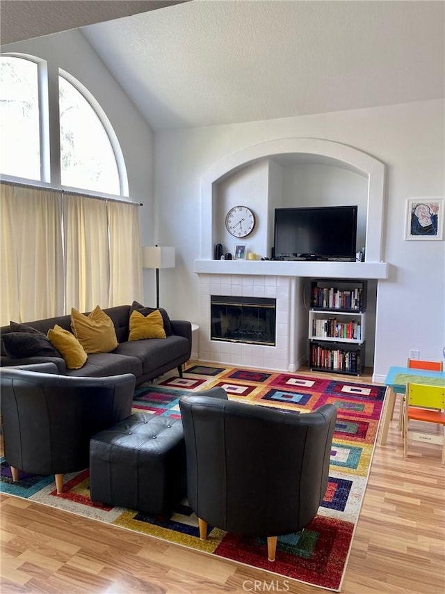 living area with lofted ceiling, a textured ceiling, a tiled fireplace, and wood finished floors