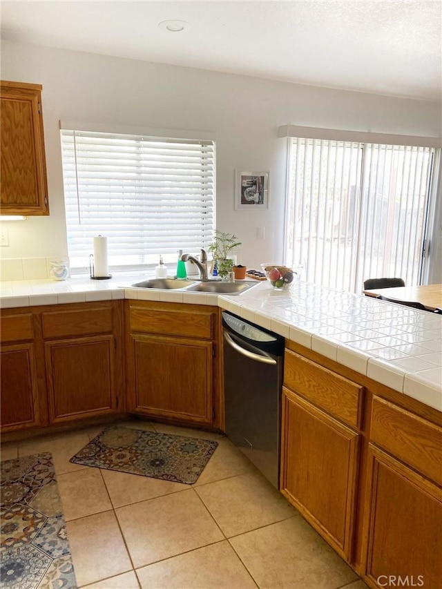 kitchen with brown cabinets, a sink, stainless steel dishwasher, and light tile patterned floors