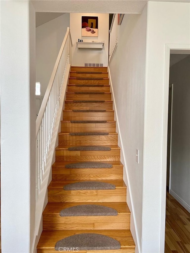 stairs featuring wood finished floors, visible vents, and baseboards