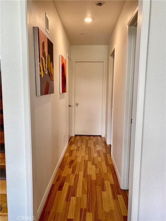 hall featuring light wood-style floors, visible vents, and baseboards