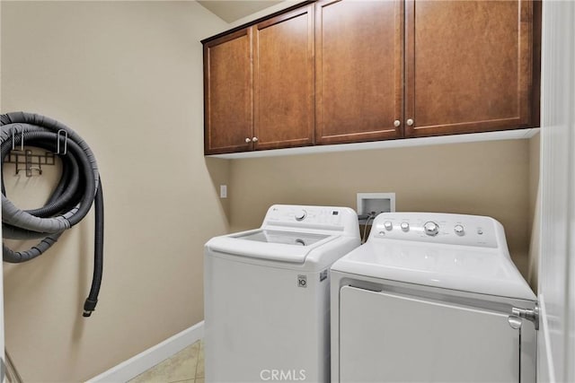 laundry area featuring washing machine and dryer, cabinet space, baseboards, and light tile patterned floors