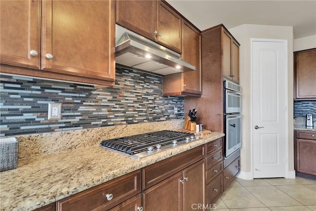 kitchen featuring light tile patterned floors, stainless steel appliances, backsplash, light stone countertops, and under cabinet range hood