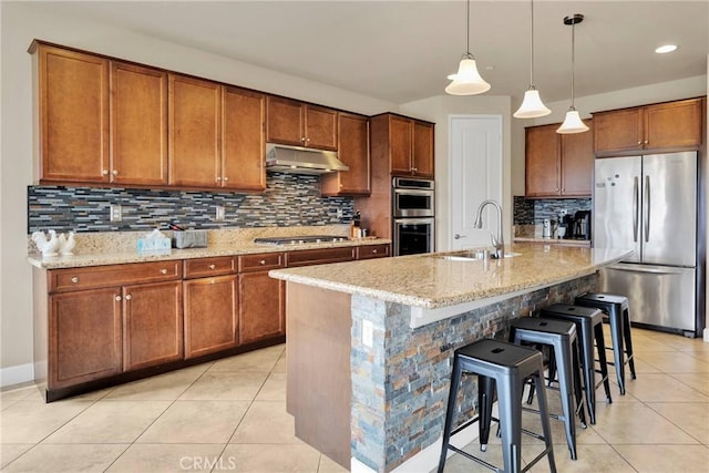 kitchen with appliances with stainless steel finishes, brown cabinetry, a sink, and under cabinet range hood