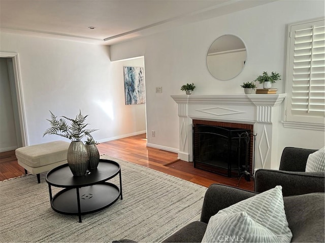 living room featuring a brick fireplace, baseboards, and wood finished floors