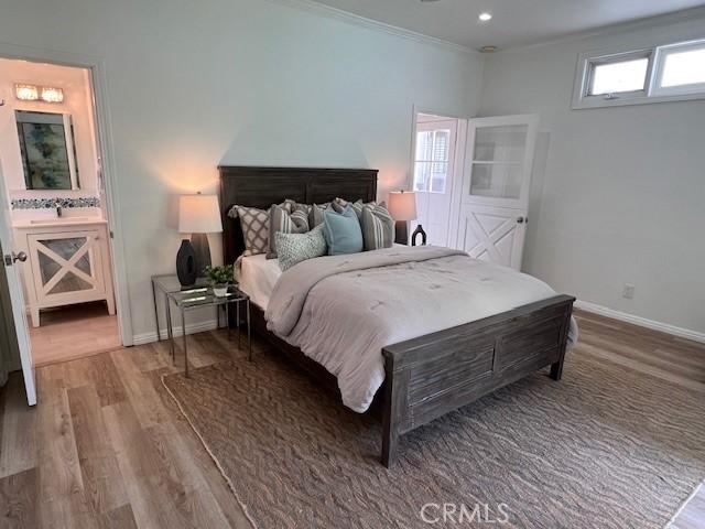 bedroom featuring baseboards, ornamental molding, wood finished floors, ensuite bathroom, and recessed lighting