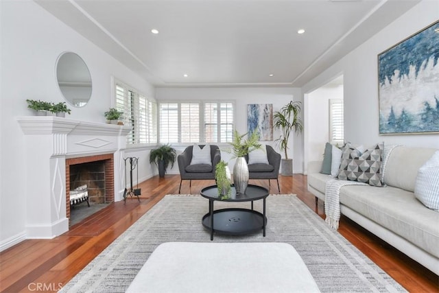 living room with recessed lighting, a brick fireplace, and wood finished floors