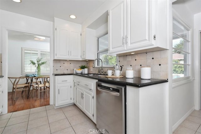 kitchen with dark countertops, stainless steel dishwasher, light tile patterned flooring, and a sink