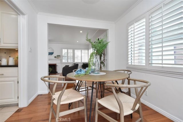 dining space with a fireplace, light wood-style flooring, and crown molding