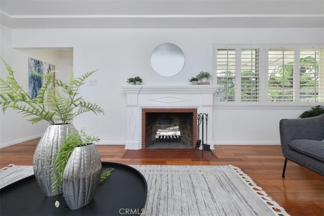 sitting room with a brick fireplace, wood finished floors, and baseboards