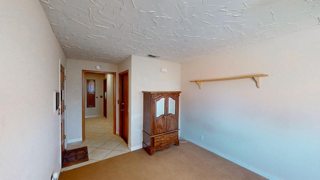 hallway featuring light tile patterned floors, light colored carpet, visible vents, and baseboards