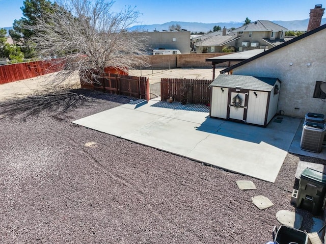 view of patio / terrace with an outbuilding, a storage shed, central AC unit, a mountain view, and a fenced backyard