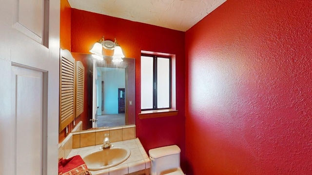 half bath featuring toilet, vanity, and a textured wall