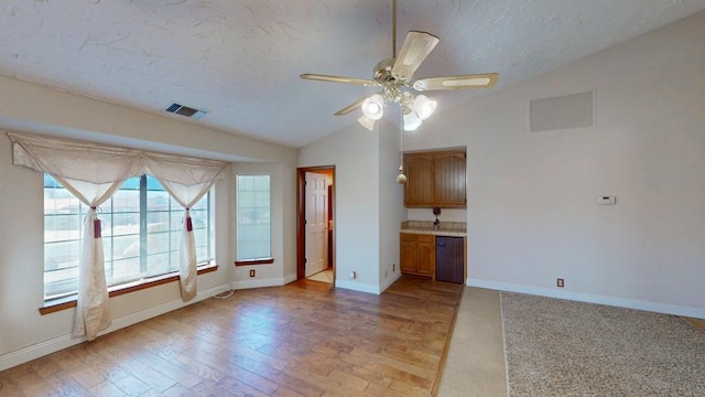 empty room featuring baseboards, visible vents, vaulted ceiling, a textured ceiling, and light wood-type flooring